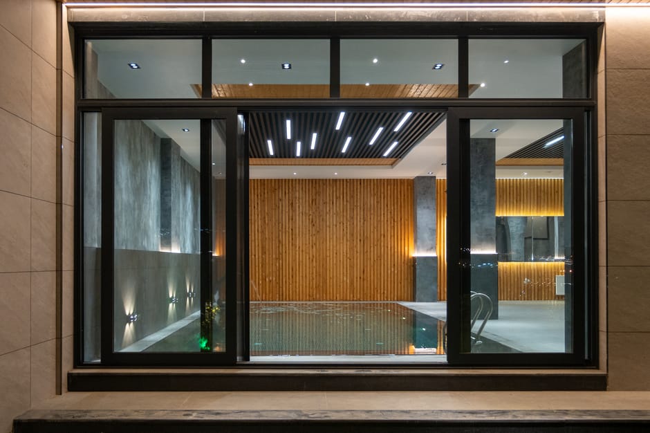 Elegant indoor pool area featuring modern lighting, wood paneling, and large glass windows for relaxation.